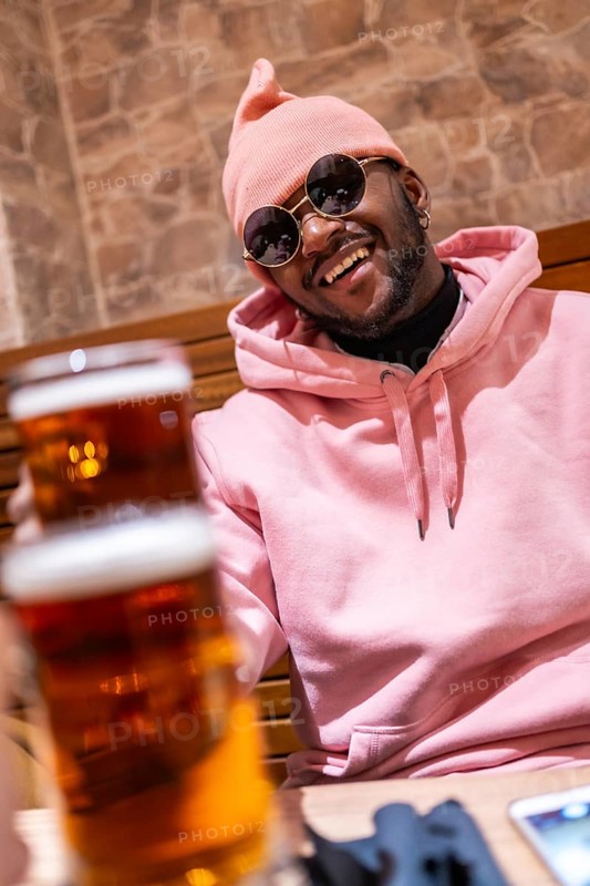 Vertical photo of a cool african man toasting with beer in a bar