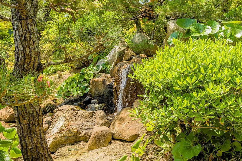 Small waterfall behind shrubbery in Japanese garden park in Hiroshima, Japan, Asia