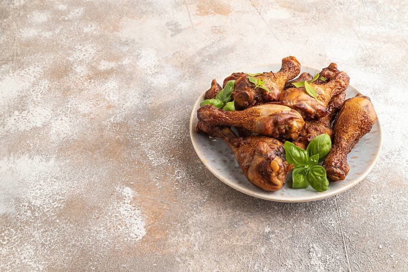Smoked chicken legs with herbs and spices on a ceramic plate on a brown concrete background. Side view, copy space