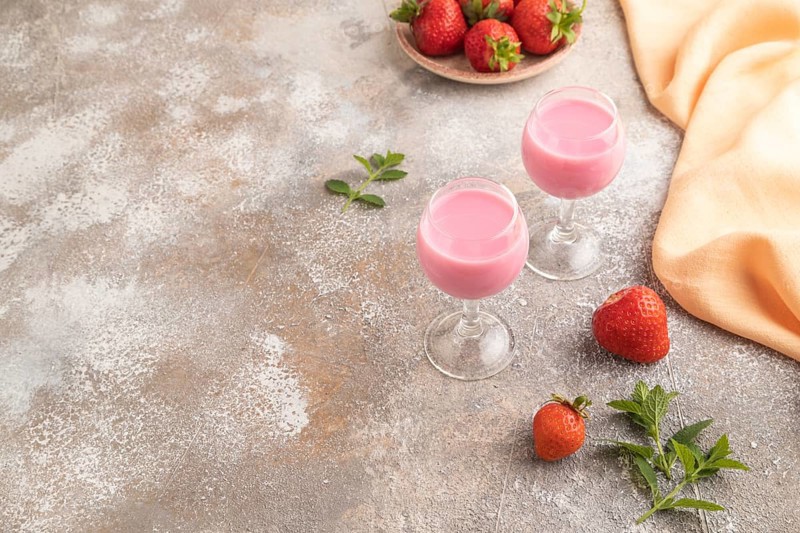 Sweet strawberry liqueur in glass on a gray concrete background and orange textile. side view, copy space