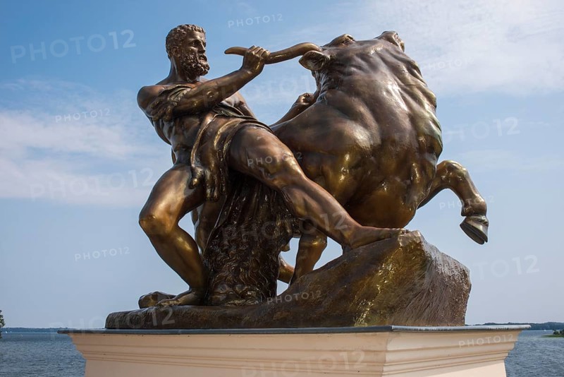 Bronzed cast zinc sculpture, statue, Heracles, taming the Cretan bull, artist: August Kriesmann, castle garden at Schwerin Castle, Schwerin's inner lake in the background, summery blue sky with light clouds, Schwerin, Mecklenburg-Western Pomerania, Germany, Europe