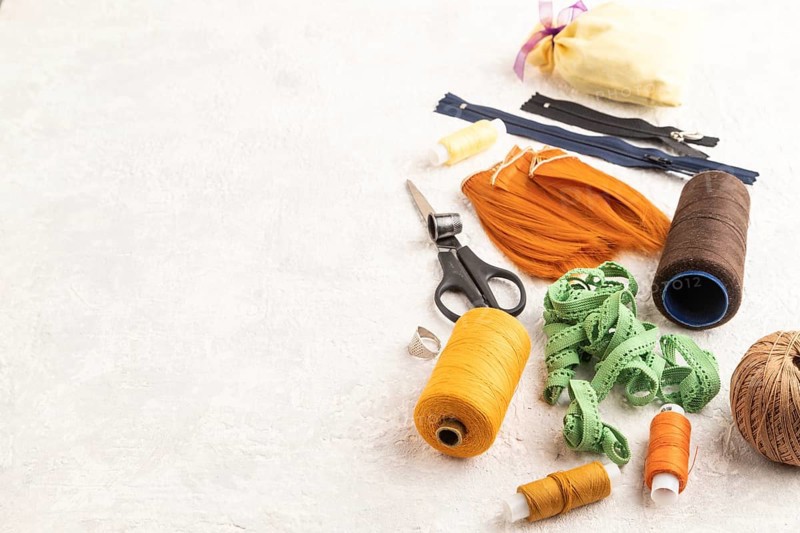 Sewing accessories: scissors, thread, thimbles, braid on gray concrete background. Side view, copy space