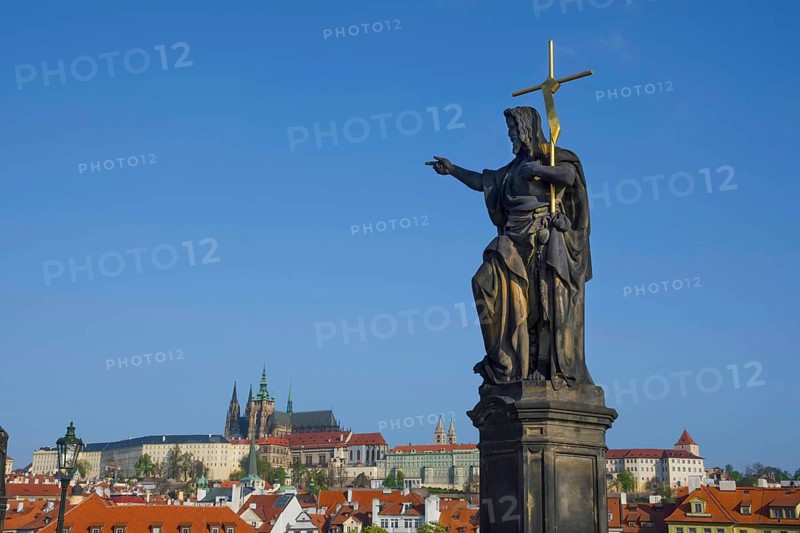 Statue of St. John the Baptist on Charles Bridge, with Hradcany castle and St. Vitus Cathedral in the background, in Prague, Czech Republic, in sunny day, Europe