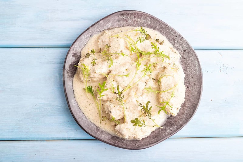 Stewed chicken fillets with coconut milk sauce and mizuna cabbage microgreen on blue wooden background. top view, flat lay, close up