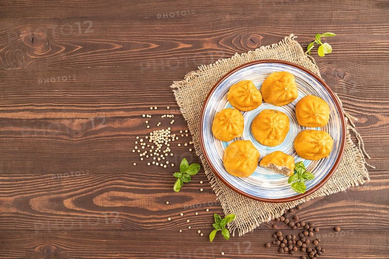 Fried manti dumplings with pepper, basil on brown wooden background and linen textile. Top view, flat lay, copy space