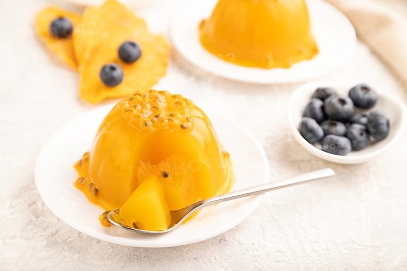 Mango and passion fruit jelly with blueberry on gray concrete background and linen textile. side view, close up, selective focus