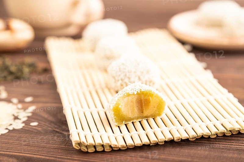 Japanese rice sweet buns mochi filled with pandan and coconut jam and cup of green tea on brown wooden background. side view, close up, selective focus