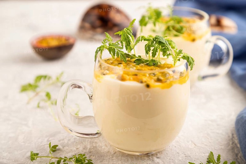 Yogurt with passionfruit and marigold microgreen in glass on gray concrete background with blue linen textile. Side view, close up, selective focus
