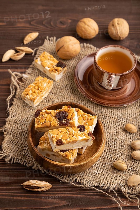 Traditional candy nougat with nuts and sesame with cup of green tea on brown wooden background and linen textile. side view, close up