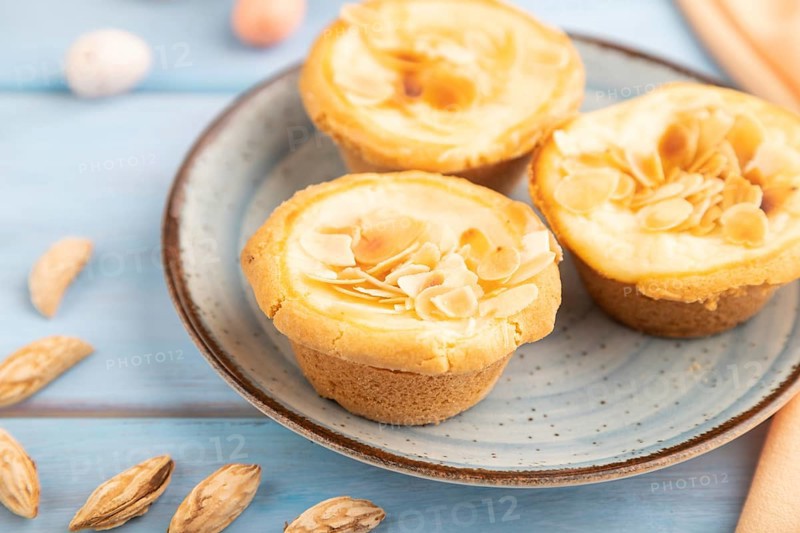 Traditional portuguese cakes pasteis de nata, custard small pies with almonds with cup of coffee on blue wooden background and orange textile. Side view, close up, selective focus