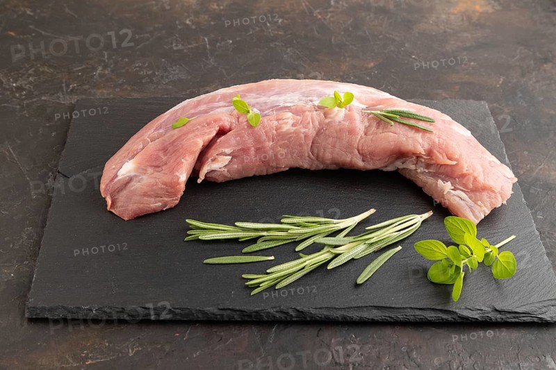Raw pork meat with herbs and spices on slate cutting board on black concrete background. Side view, close up