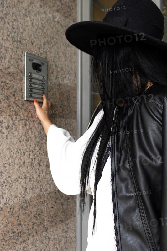 Vertical Side view of unrecognizable woman wearing a hat pushing the button of the intercom of building