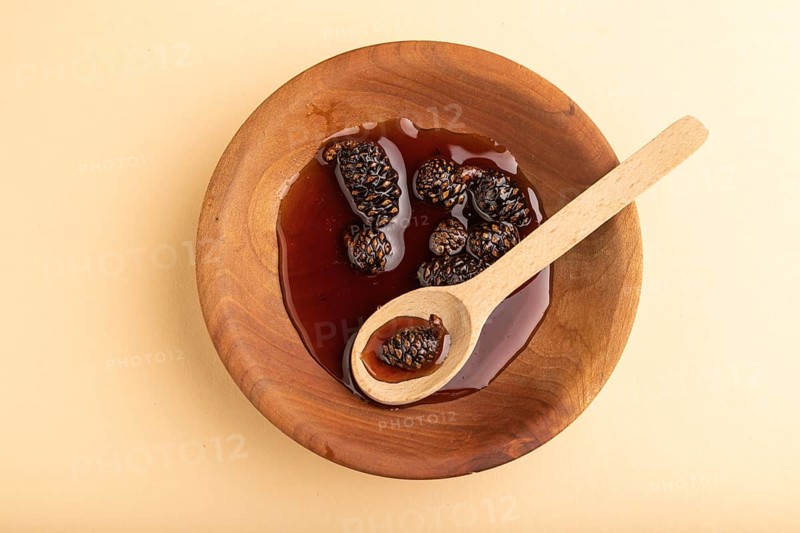 Pine cone jam in wooden bowl on orange pastel background. Top view, flat lay, close up