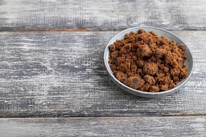 Plate with unrefined brown cane sugar on gray wooden background. side view, copy space