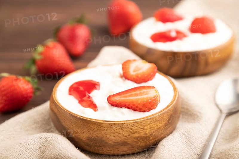 Grained cottage cheese with strawberry jam on brown wooden background and linen textile. side view, close up, selective focus