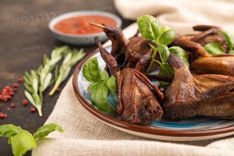 Smoked quails with herbs and spices on a ceramic plate with linen textile on a black concrete background. Side view, close up, selective focus
