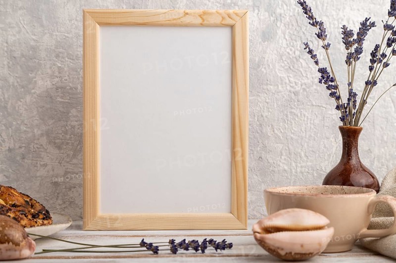 White wooden frame mockup with lavender in ceramic vase, linen textile, cup of coffee and bun on gray concrete background. Blank, vertical orientation, still life