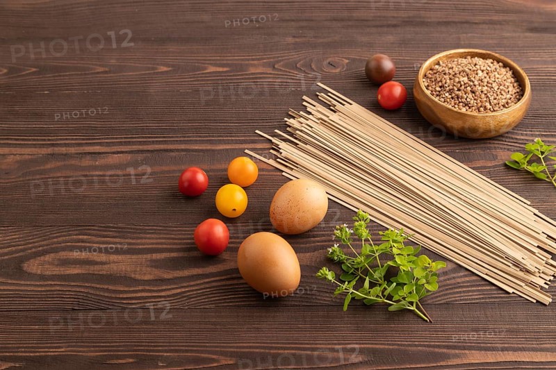 Japanese buckwheat soba noodles with tomato, eggs, spices, herbs on brown wooden background. Side view, copy space