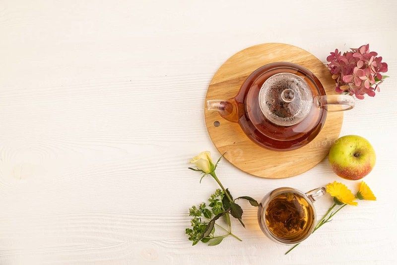 Red tea with herbs in glass teapot on white wooden background. Healthy drink concept. Top view, flat lay, copy space