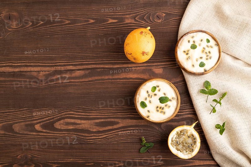 Yoghurt with granadilla and mint in wooden bowl on brown wooden background and linen textile. top view, flat lay, copy space