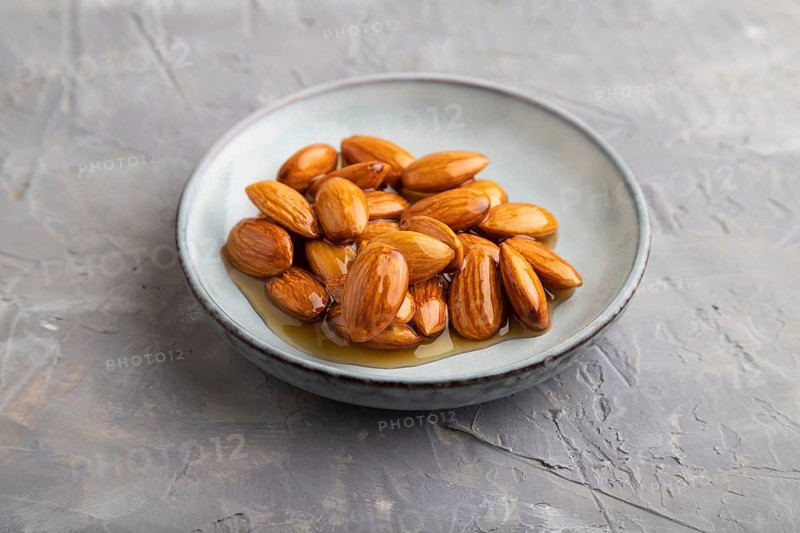 Almonds with honey on gray concrete background. side view, close up