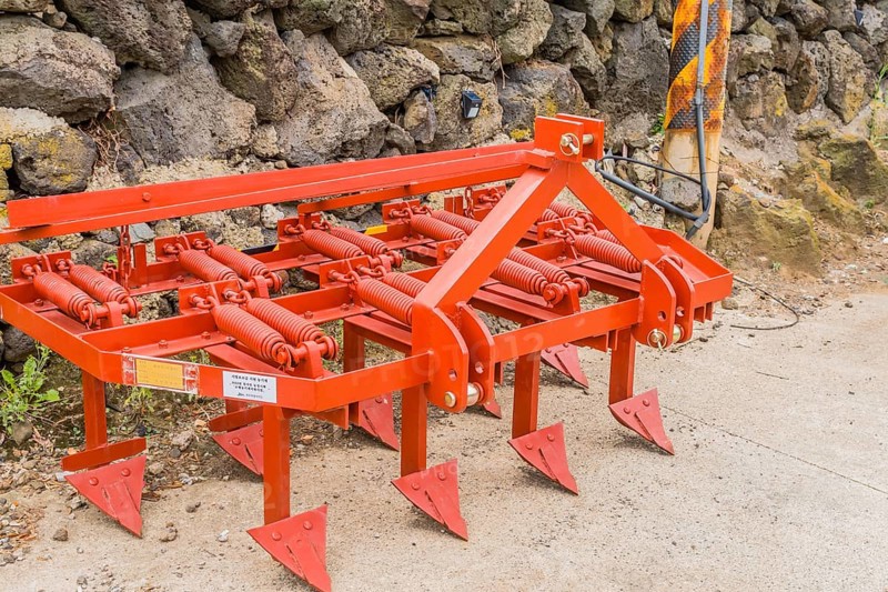 Bright orange plow resting against stone wall in Jeju, South Korea, Asia