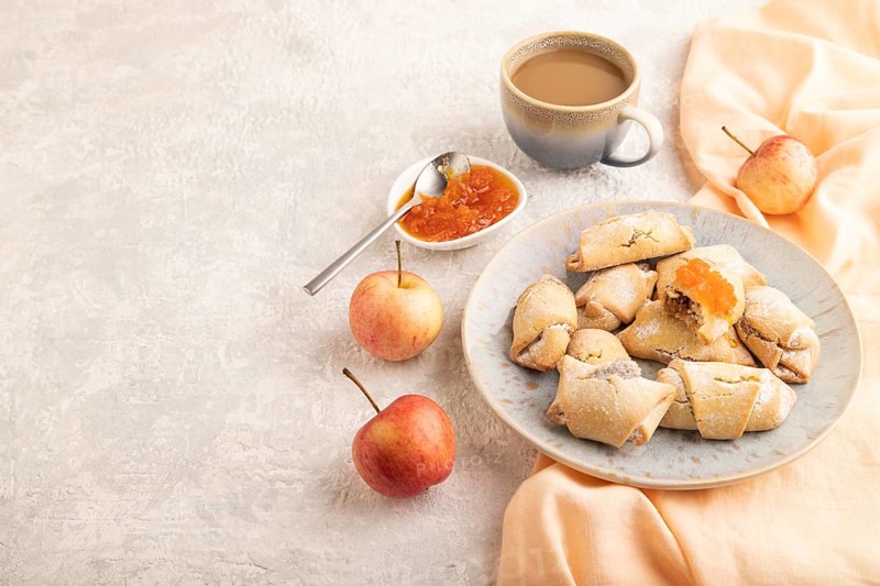 Homemade sweet cookie with apple jam and cup of coffee on gray concrete background and orange linen textile. side view, copy space