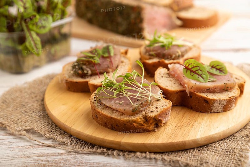 Bread sandwiches with jerky salted meat, sorrel and cilantro microgreen on white wooden background and linen textile. side view, close up, selective focus