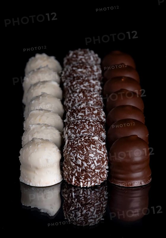 Row of chocolate kisses covered with dark and light chocolate, grated coconut, reflection, dark background