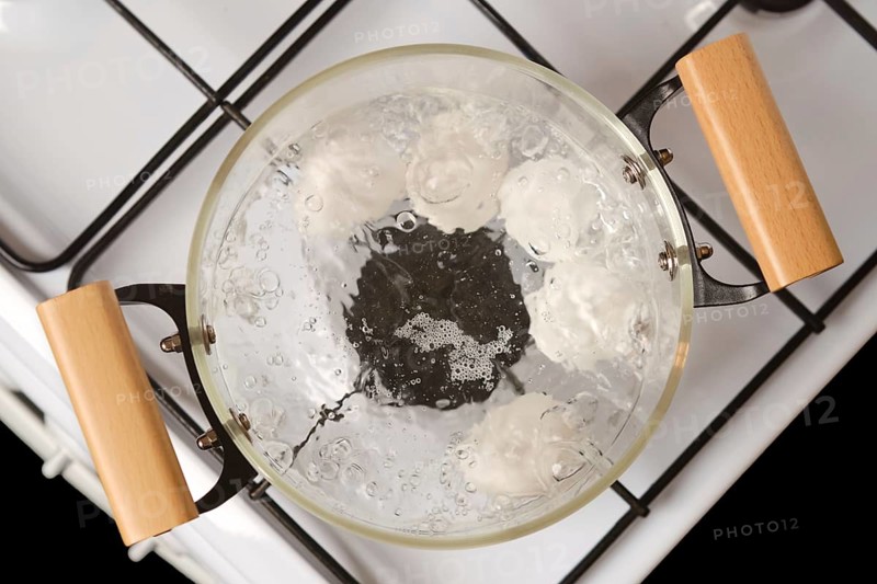 Overhead closeup view of transparent glass saucepan with boiling eggs on a gas stove