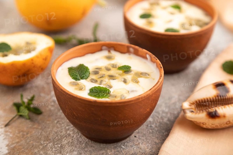 Yoghurt with granadilla and mint in clay bowl on brown concrete background and orange linen textile. side view, close up, selective focus