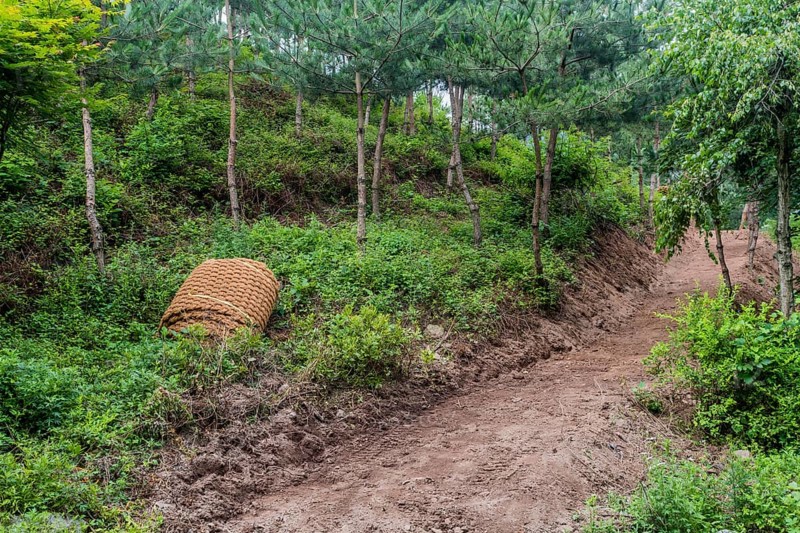 Thatch rope mat laying rolled up on ground near freshly excavated hiking trail in South Korea