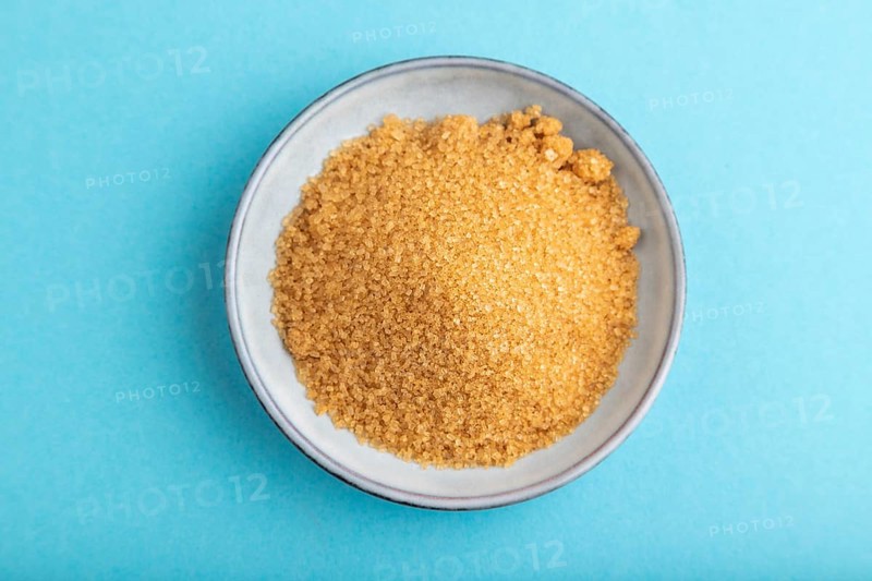 Plate with unrefined golden cane sugar on blue pastel background. top view, flat lay, close up