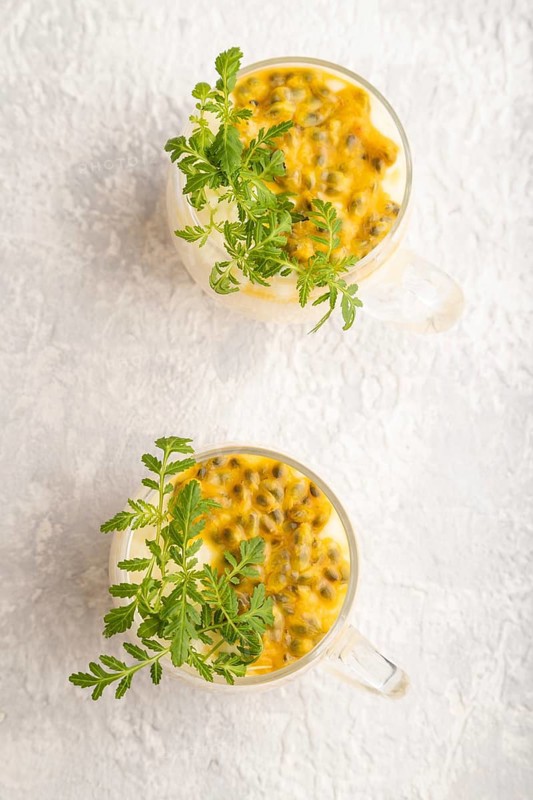 Yogurt with passionfruit and marigold microgreen in glass on gray concrete background. Top view, flat lay, close up