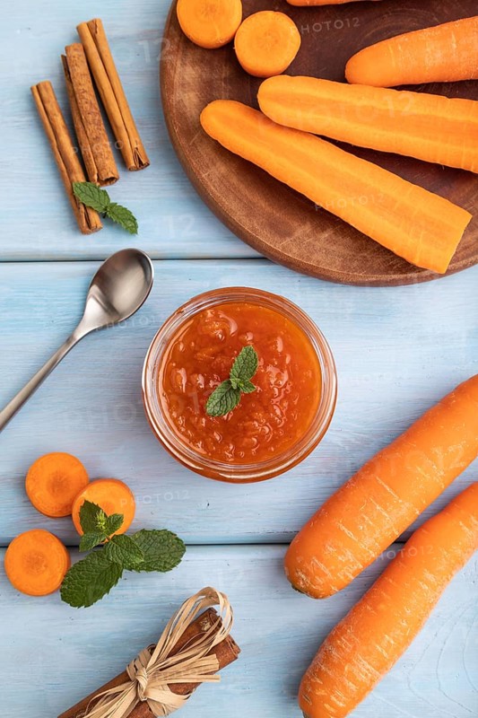 Carrot jam with cinnamon in glass jar on blue wooden background. Top view, flat lay, close up