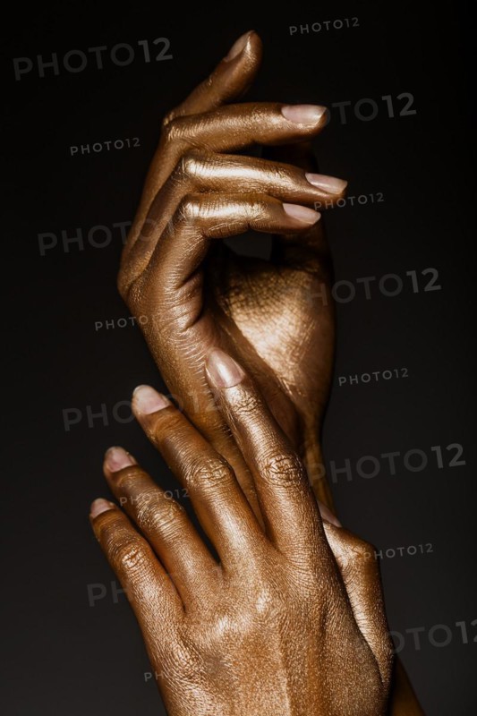 Beautiful man's hands in golden paint on black background close up