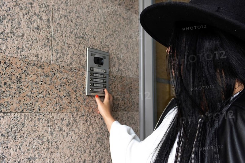 Side view of unrecognizable woman wearing a hat pushing the button of the intercom of building