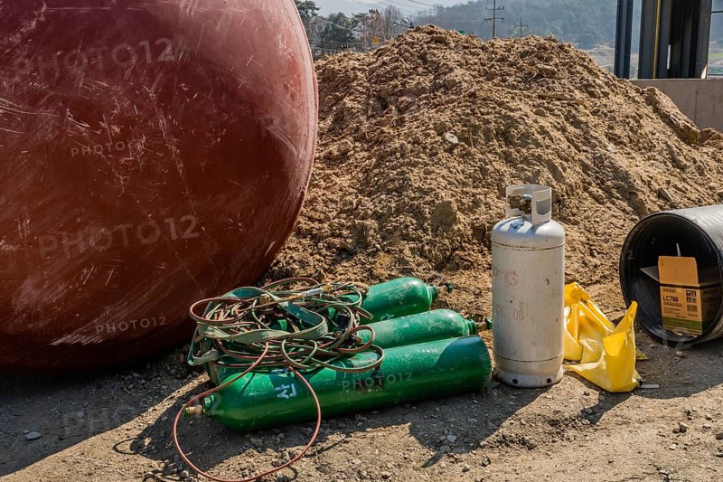 Chungju, South Korea, March 22, 2020: For editorial use only. Welding oxygen tanks and equipment laying on ground beside large metal container at construction site, Asia