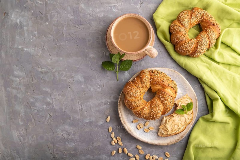 Homemade sweet bun with peanut butter and cup of coffee on a gray concrete background and green linen textile. top view, flat lay, copy space