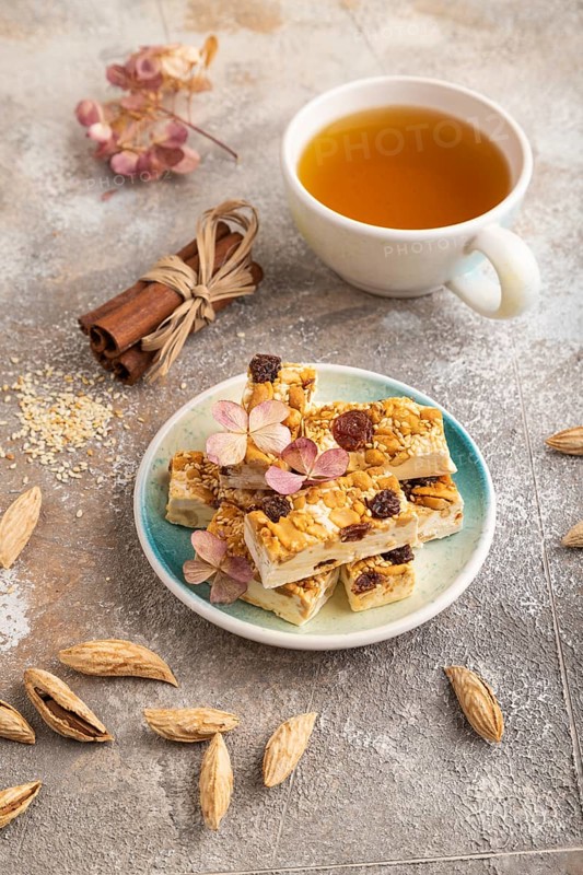 Traditional candy nougat with nuts and sesame with cup of green tea on brown concrete background. side view, close up