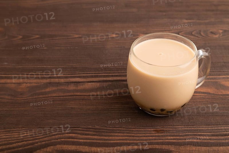 Bubble tea with pistachio and caramel in glass on brown wooden background. Healthy drink concept. Side view, copy space