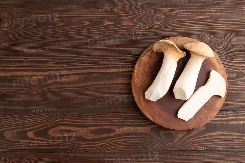 King Oyster mushrooms or Eringi (Pleurotus eryngii) on brown wooden background. Top view, flat lay, copy space