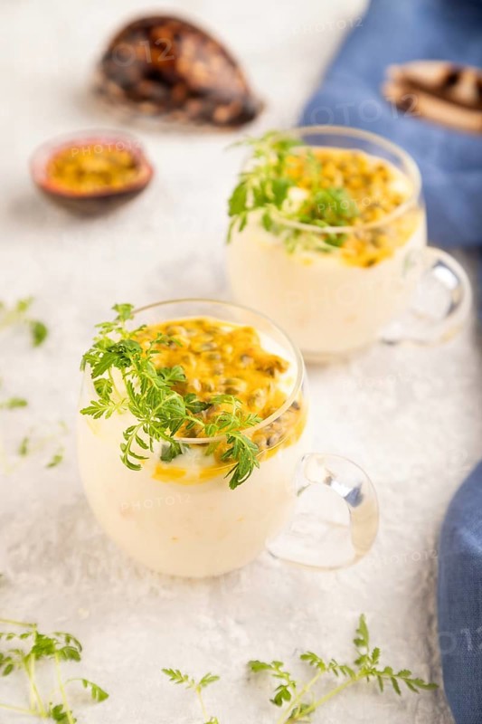Yogurt with passionfruit and marigold microgreen in glass on gray concrete background with blue linen textile. Side view, close up, selective focus