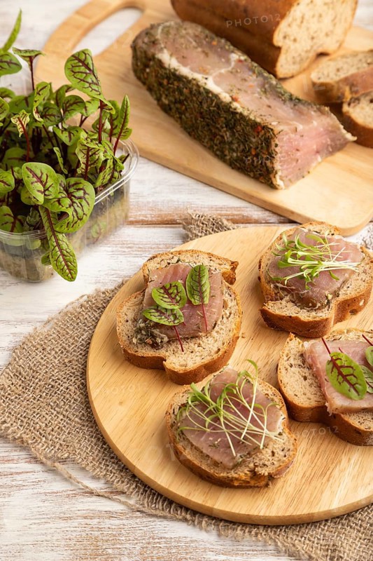 Bread sandwiches with jerky salted meat, sorrel and cilantro microgreen on white wooden background and linen textile. side view, close up
