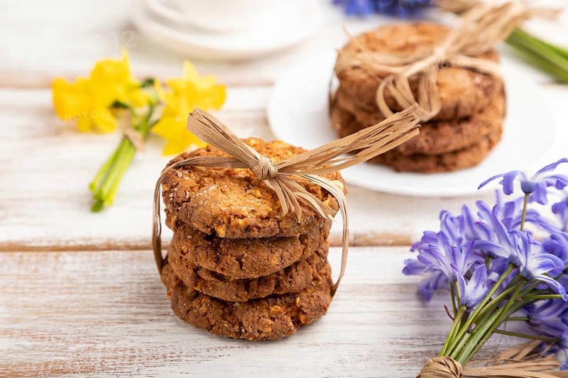 Oatmeal cookies with spring snowdrop flowers bluebells, narcissus and cup of coffee on white wooden background. side view, close up, still life. Breakfast, morning, spring concept