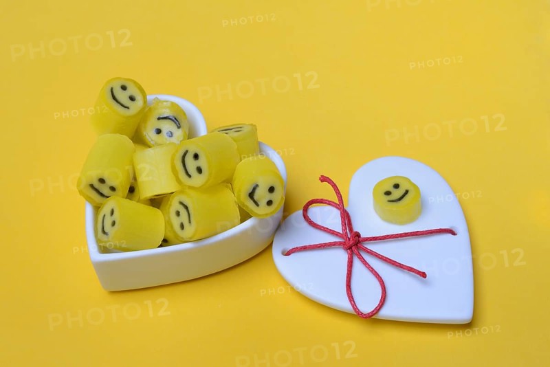 Yellow sweets with smiley in a heart-shaped bowl