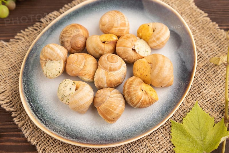 Grape (Burgundy) snails with butter and cheese on brown wooden background and linen textile. Side view, selective focus