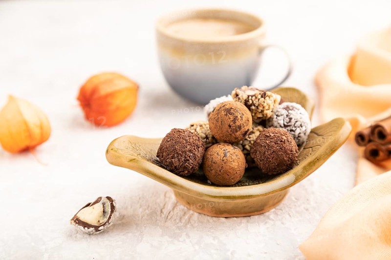 Chocolate truffle candies with cup of coffee on a gray concrete background and orange textile. side view, close up, selective focus
