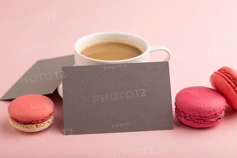 Gray paper business card mockup with red and purple macaroons and cup of coffee on pink pastel background. Blank, side view, copy space, still life, close up. morning, breakfast concept