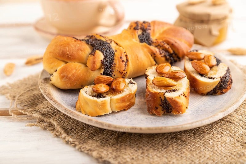 Homemade sweet bun with honey almonds and cup of green tea on a white wooden background and linen textile. side view, close up, selective focus
